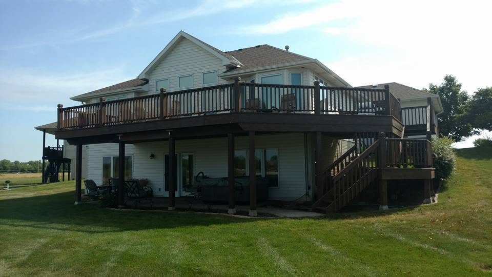 Modern two-story house with wraparound dark deck, white siding, and manicured lawn