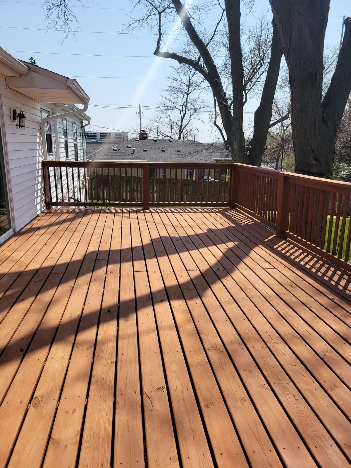 Newly stained wooden deck with brown railing overlooking residential neighborhood on sunny day