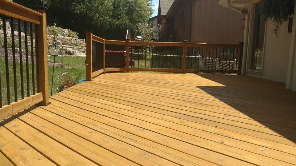 Newly stained wooden deck with metal railings and gate attached to residential home