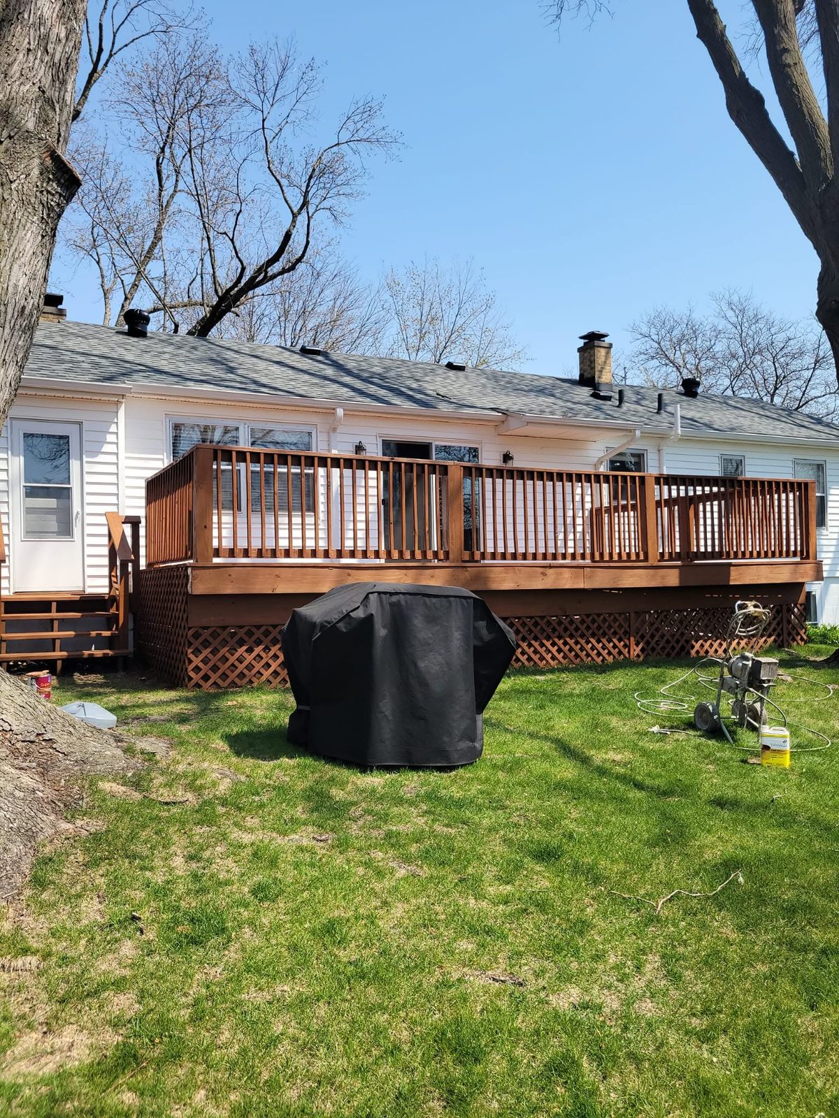 Single-story home with wooden deck, black grill cover on grass, bare trees visible