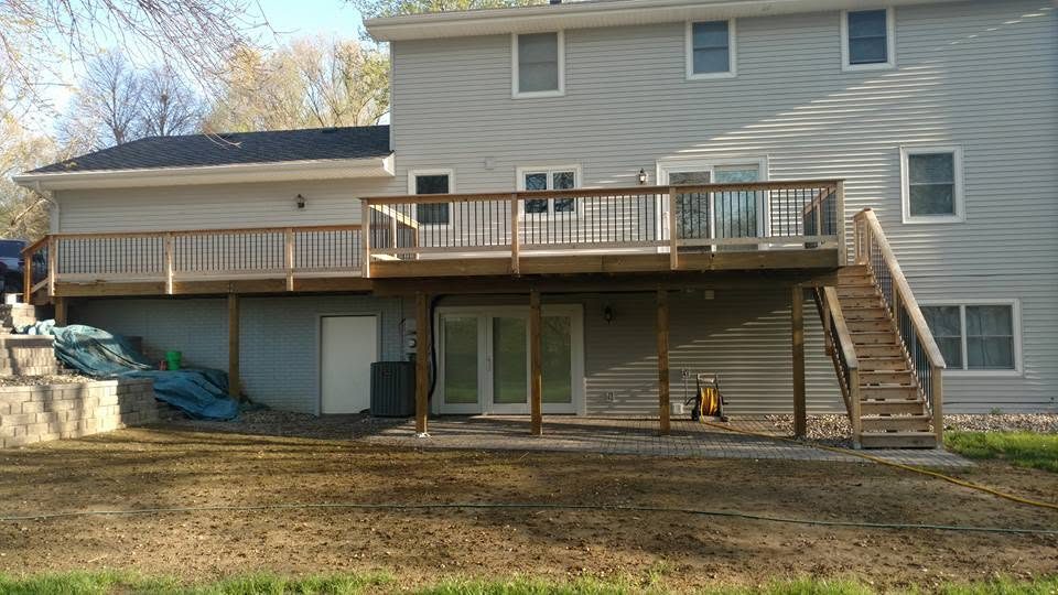 Two-story house with wooden deck and metal railing overlooking bare yard