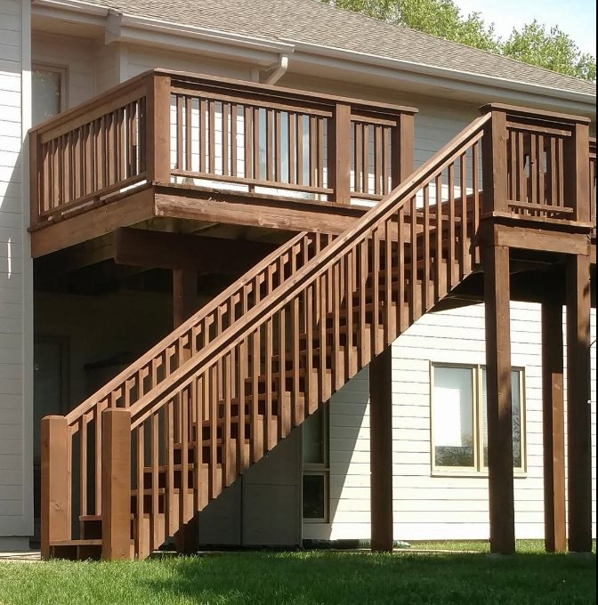 Two-story wooden deck with staircase and vertical railings on residential home
