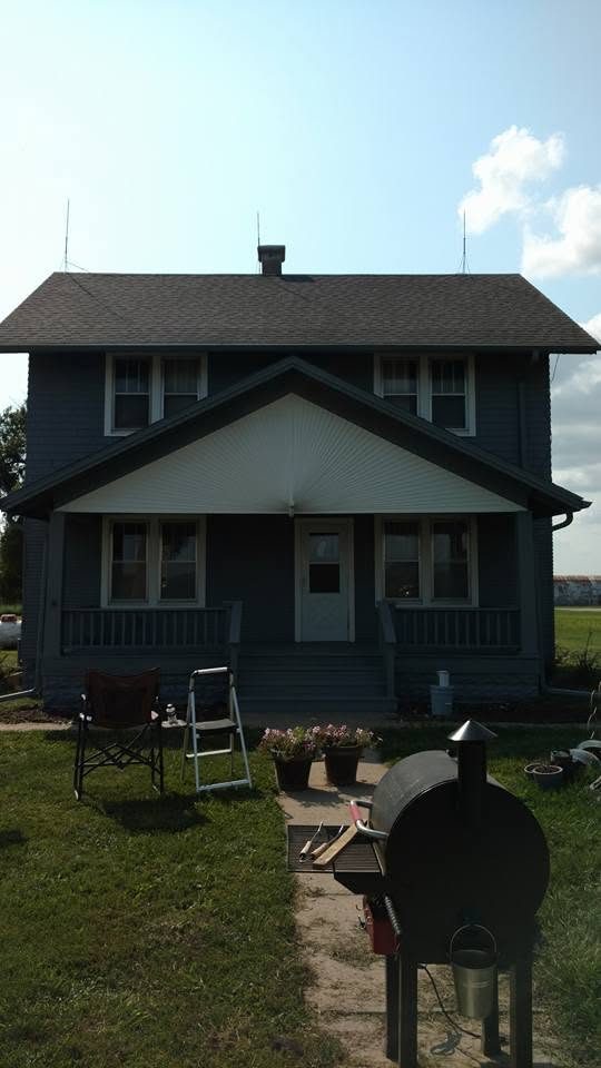 Dark blue two-story farmhouse with white gable and front porch, BBQ grill in foreground