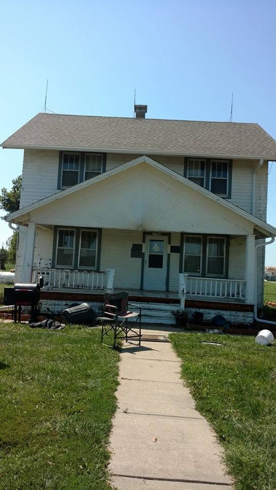 White two-story farmhouse with front porch and gray roof against clear sky