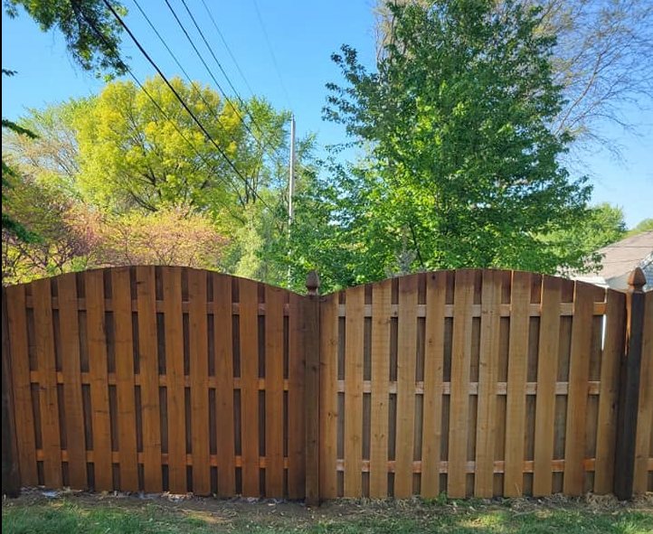 Two wooden privacy fences with curved tops in a residential yard with green trees