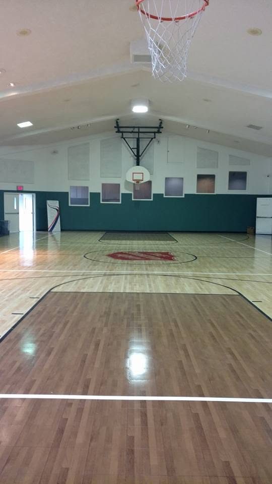 Indoor gymnasium with wooden floor, basketball hoops, and green wall paneling