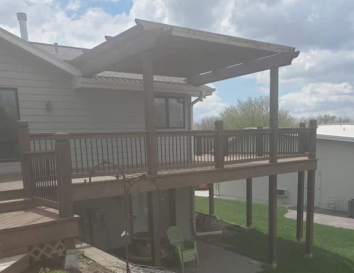Two-tier deck with pergola shade structure and metal railings attached to residential home