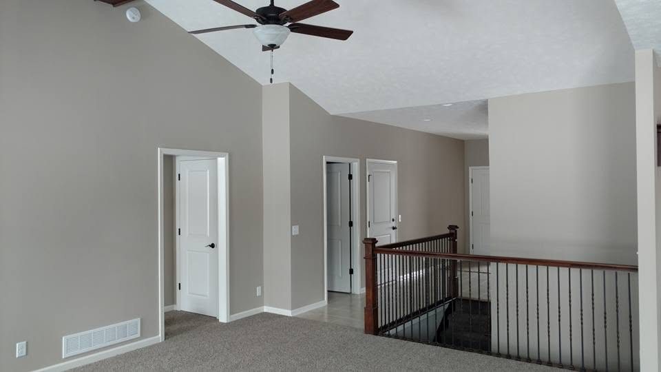 Spacious upstairs loft with beige walls, ceiling fan, carpet flooring, and wooden stair railing